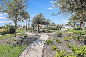 A residential area with a paved walkway, trees, and houses in the background.
