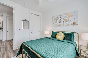 A bedroom with a teal bedspread, a gold-framed headboard, and a floral artwork on the wall.