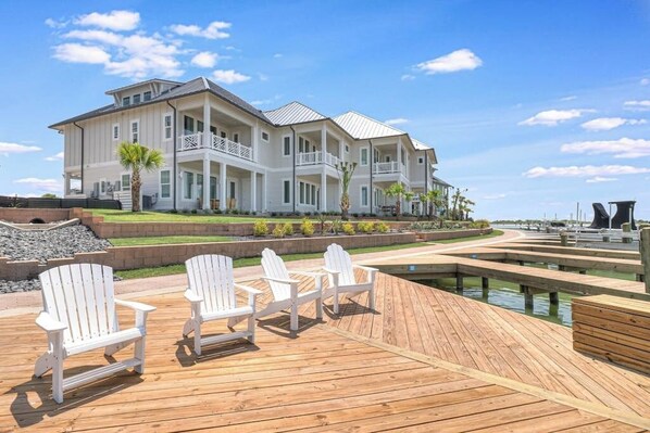 A waterfront property with a large house, a wooden deck with chairs, and a marina.