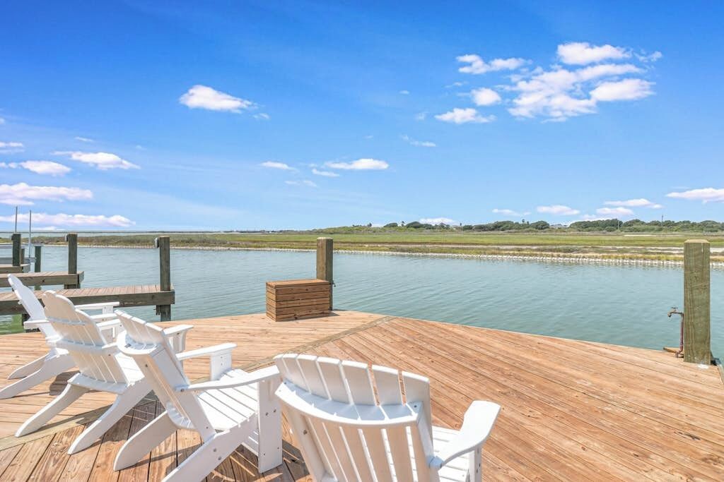Eine Holzterrasse mit weißen Stühlen mit Blick auf ruhiges Wasser.