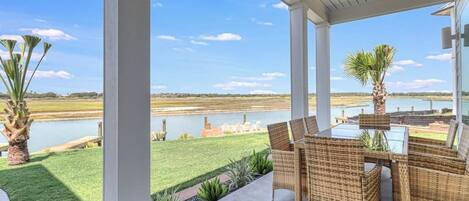 An outdoor patio with wicker furniture, a view of a lake, and a grassy area.
