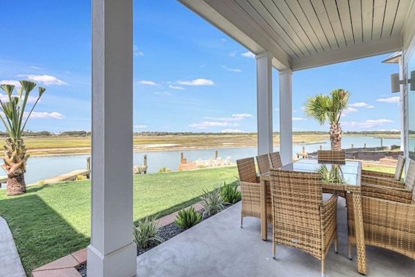 An outdoor patio with wicker furniture, a view of a lake, and a grassy area.