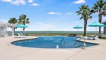 A swimming pool with lounge chairs and umbrellas, surrounded by palm trees and a clear sky.