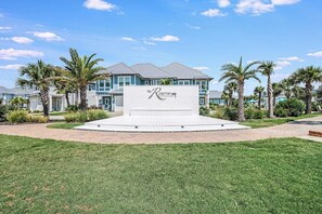 A hotel entrance with a central sign, surrounded by a well-maintained lawn and palm trees.