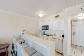 A compact kitchen with white cabinets, a microwave, a sink, and a small dining area with chairs. - Beachfront Haven - Gulf-Front, Pool & Hot Tub (Galveston)