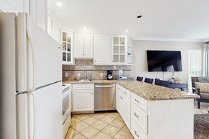 A modern kitchen with white cabinets, a granite countertop, and a built-in dishwasher. - Seascape Gem - Ocean-View Balcony, Pool & Hot Tub (Galveston)