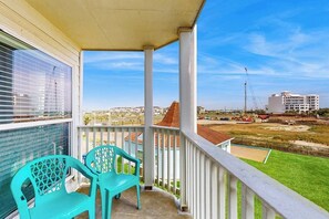 A balcony with two chairs, a view of a cityscape, and a clear sky. - Seascape Gem - Ocean-View Balcony, Pool & Hot Tub (Galveston)