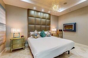 A modern bedroom with a large bed, two bedside tables, a decorative ceiling light, and a framed picture on the wall. - Diamond Beach Crown Jewel - #714 (Galveston)