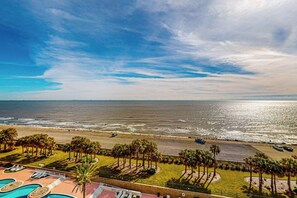 A beachfront hotel with a pool, palm trees, and a view of the ocean. - Diamond Beach Crown Jewel - #714 (Galveston)