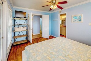 A bedroom with a bed, a ceiling fan, a TV on a stand, and a door leading to another room. - Seascape Condos #1222 (Galveston)