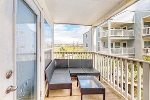 A balcony with a sofa and table, a white railing, and a view of a residential area. - Seascape Condos #1222 (Galveston)