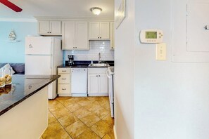 A kitchen with white cabinets, a refrigerator, a stove, and a sink. There is a thermostat on the wall. - Seascape Condos #1222 (Galveston)