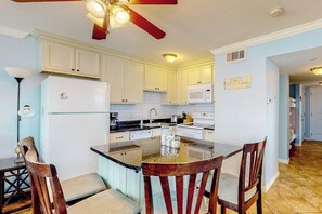 A kitchen with white cabinets, a central island with chairs, a ceiling fan, and a microwave. - Seascape Condos #1222 (Galveston)