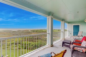 A covered porch with a view of a coastal landscape, furnished with chairs and a table. - Pointe West Retreat Unit 302 (Galveston)