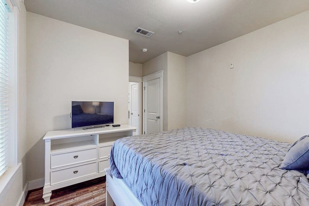 Un dormitorio con una cama, un televisor sobre un tocador blanco y una puerta al fondo.