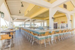 A covered outdoor bar area with multiple seating options, including bar stools and chairs, and a central bar counter. - Pointe West Retreat Unit 302 (Galveston)