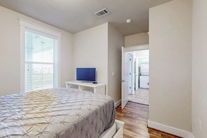 A bedroom with a bed, a television on a stand, and a door leading to another room. - Pointe West Retreat Unit 302 (Galveston)