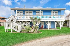 A two-story house with a porch, stairs, and a small garden. - Seaside Cottage - Bayfront, Dock & Dog-Friendly (Galveston)