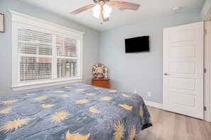A bedroom with a bed, a ceiling fan, a television on the wall, and a door. - Seaside Cottage - Bayfront, Dock & Dog-Friendly (Galveston)