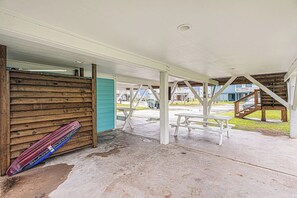 An outdoor covered area with a picnic table and benches, a wooden bench, and a skateboard leaning against a wall. - Seaside Cottage - Bayfront, Dock & Dog-Friendly (Galveston)