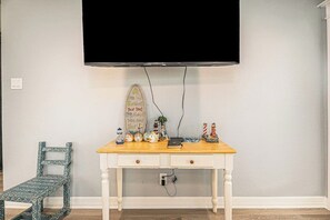 A room with a white desk, a television mounted on the wall, and a small chair. - Seaside Cottage - Bayfront, Dock & Dog-Friendly (Galveston)