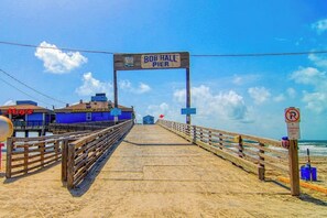 A pier with a sign reading 'Bob Hall Pier' leading to a beachside bar and grill. - Leeward Cove B4 - Pool & Bay Views, Dogs Welcome (Corpus Christi)