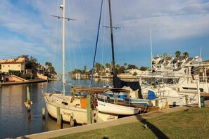 A marina with boats docked, a grassy area in the foreground, and buildings in the background. - Leeward Cove B4 - Pool & Bay Views, Dogs Welcome (Corpus Christi)