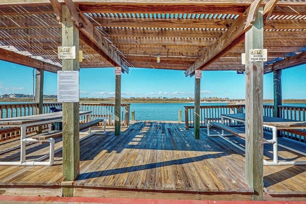 Eine hölzerne Pier mit Bänken und einem überdachten Bereich, mit Blick auf ein Gewässer.