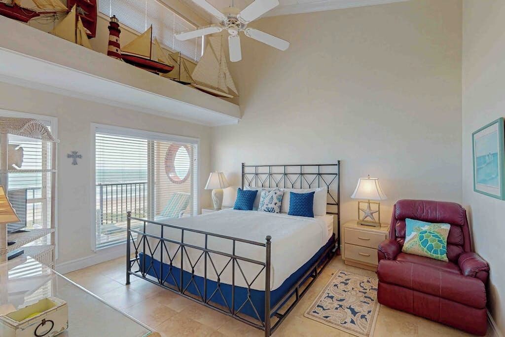 A bedroom with a bed, a ceiling fan, a red chair, and a window with blinds.