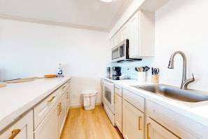 A compact kitchen with white cabinets, a stainless steel sink, and a microwave. - Florence Condominiums #303 (South Padre Island)