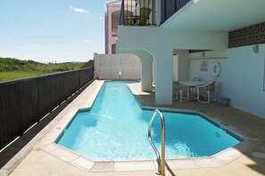 A swimming pool with a metal ladder, surrounded by a concrete deck, and a small seating area with chairs and a table. - Florence Condominiums #303 (South Padre Island)