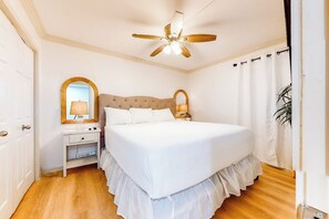 Une chambre à coucher avec un grand lit, un ventilateur de plafond, une table de chevet avec une lampe et un miroir.