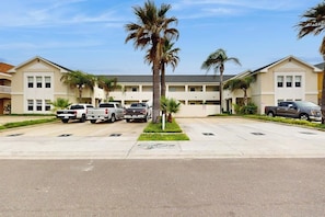 A motel with a parking lot, several parked vehicles, and palm trees. - Dancing Turtle Cay - Pool, Walkable to the Beach (South Padre Island)