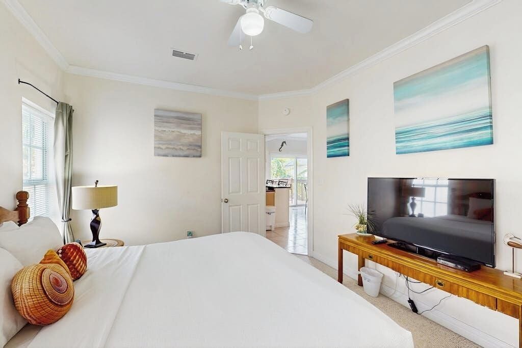 Ein Hotelzimmer mit Bett, Fernseher, Deckenventilator und Bildern an den Wänden.