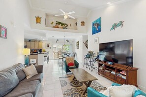 A spacious living area with a sofa, coffee table, TV, and artwork on the walls. - Dancing Turtle Cay - Pool, Walkable to the Beach (South Padre Island)