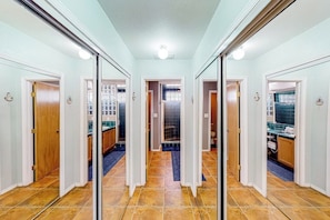 A hallway with mirrored doors leading to a bathroom and a kitchen area. - Cora Lee - Private Pool & Putting Green (South Padre Island)