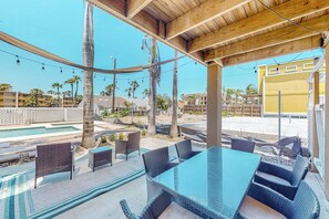 An outdoor patio with wicker furniture, a glass table, and a pool in the background. - Cora Lee - Private Pool & Putting Green (South Padre Island)