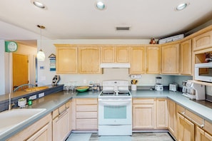A kitchen with wooden cabinets, a white stove, and various appliances. - Cora Lee - Private Pool & Putting Green (South Padre Island)