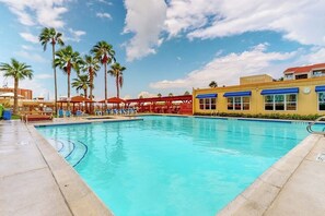 A swimming pool with lounge chairs, palm trees, and a building with a yellow facade. - Gulfview I #201 - Pool & Hot Tub, Near the Beach (South Padre Island)