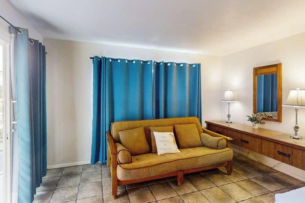 Ein Zimmer mit einer Couch, Vorhängen, einem Spiegel und einer Lampe.