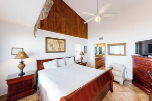 A bedroom with a large bed, wooden headboard, a ceiling fan, a television, and a dresser. - Suntide II Condominiums #509 (South Padre Island)