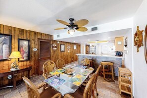 A dining area with a wooden table and chairs, a ceiling fan, and a kitchen in the background. - Suntide II Condominiums #509 (South Padre Island)