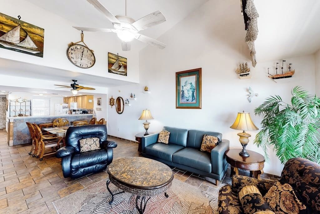 A living room with a blue sofa, a leather armchair, a coffee table, and a dining area with wooden chairs.