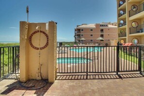 A gated pool area with a view of a multi-story building in the background. - Suntide II Condominiums #509 (South Padre Island)