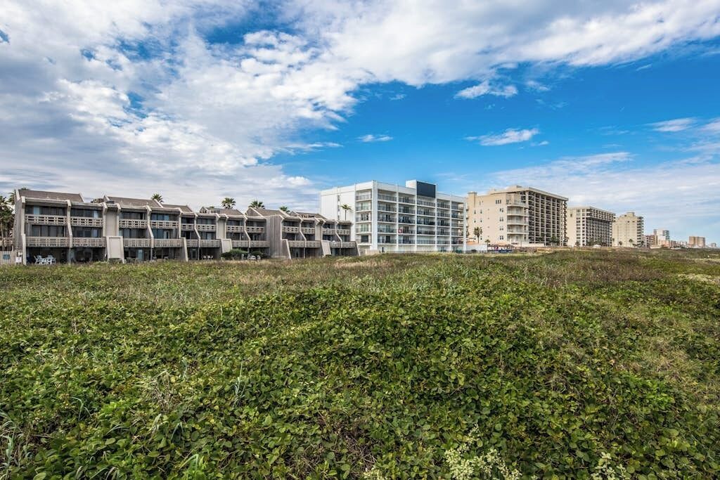 A modern hotel complex with multiple buildings, a grassy foreground, and a clear sky.