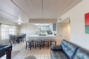 A modern living room with a sofa, a dining area with chairs, a kitchen with cabinets, and a bar area with stools. - Fiesta Sol Condominiums 212 (South Padre Island)