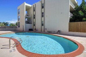 A swimming pool with a metal ladder, surrounded by a brick edge, adjacent to a multi-story building with balconies. - Fiesta Sol Condominiums 212 (South Padre Island)