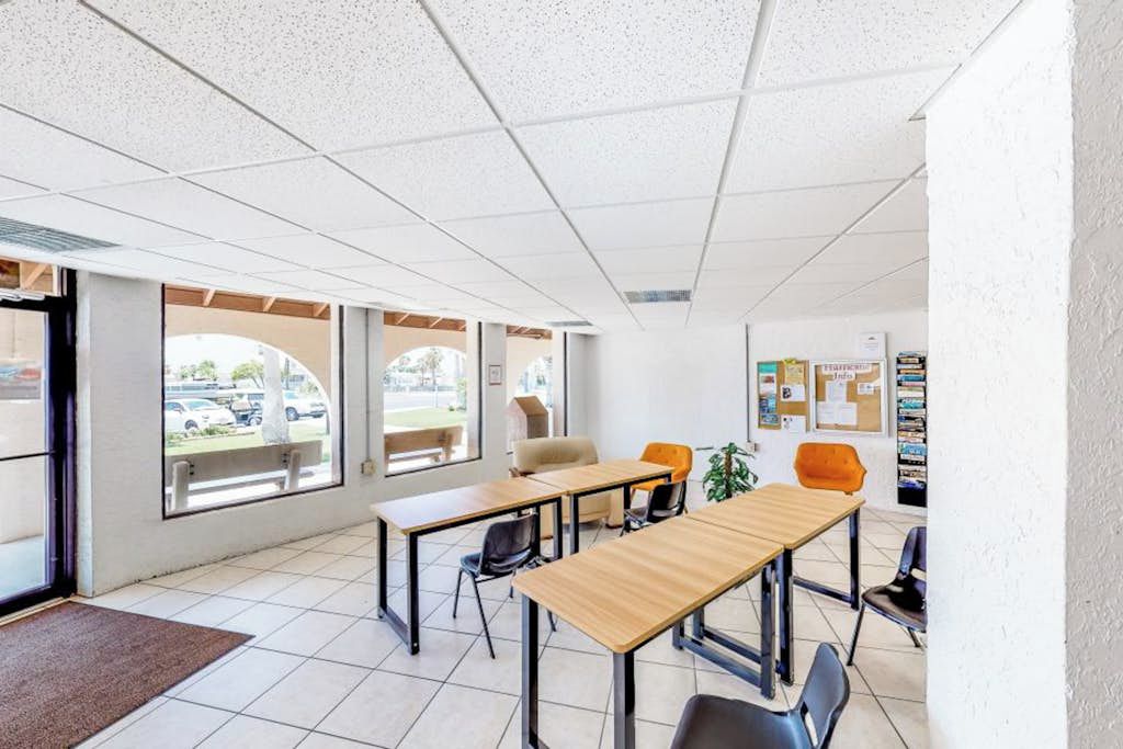 A modern classroom with large windows, white walls, and a bulletin board.