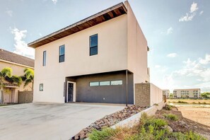 A modern two-story house with a garage, a driveway, and a landscaped front yard. - Harbor Island Beach House #1533 (Port Isabel)