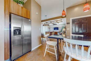 Une cuisine moderne dotée d’appareils électroménagers en acier inoxydable, un coin repas avec des chaises blanches et un éclairage suspendu.